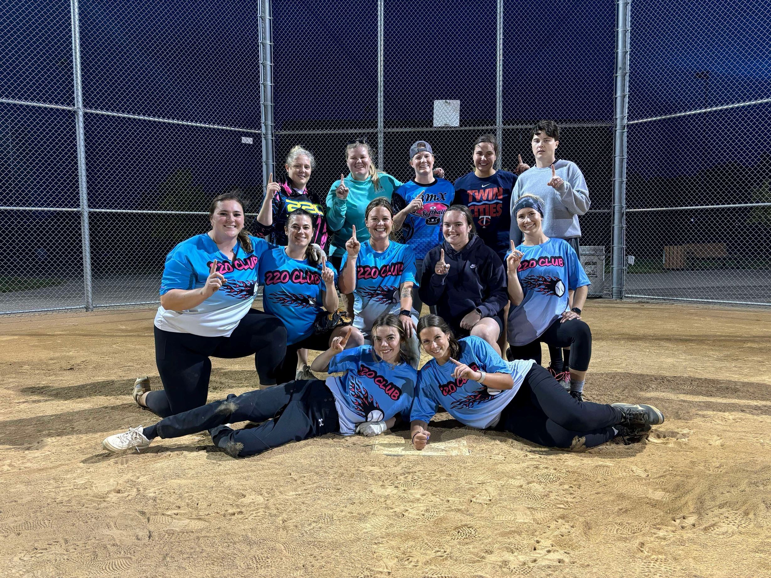 Women's adult softball team. 12 women standing behind home plate. 